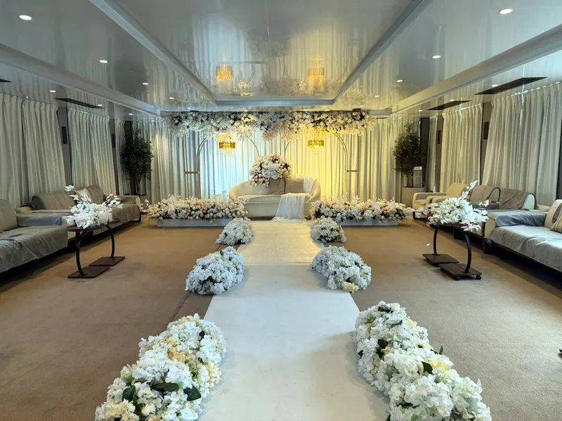 Longue allée blanche bordée de compositions de fleurs blanches dans une salle drapée
