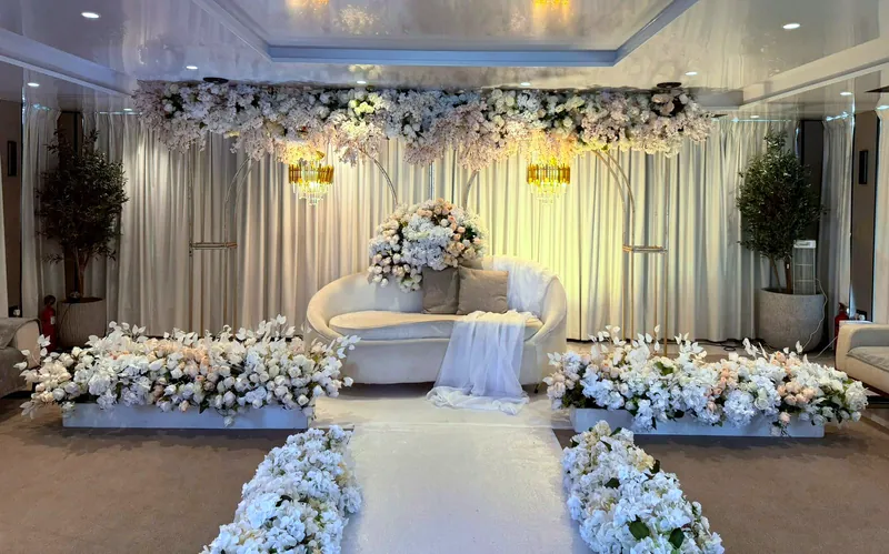 Allée fleurie blanche menant à une scène avec un sofa, des fleurs blanches et des lumières douces