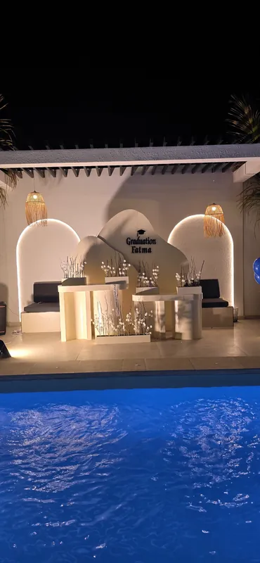 Arches blanches et table dressée éclairée au bord d’une piscine, la nuit