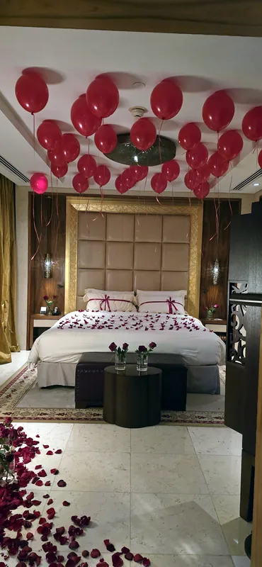 Chambre décorée de ballons rouges, de pétales de roses et d’un lit avec un cœur de pétales