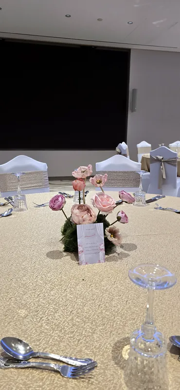 Table d’invités avec des roses roses, un menu et des couverts argentés